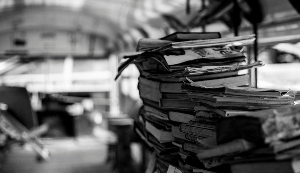 Greyscale photo of a stack of old books and papers in a room