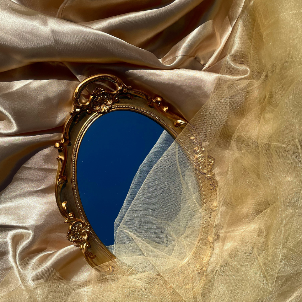 Antique mirror resting on a bed of satin partly covered by gold tulle